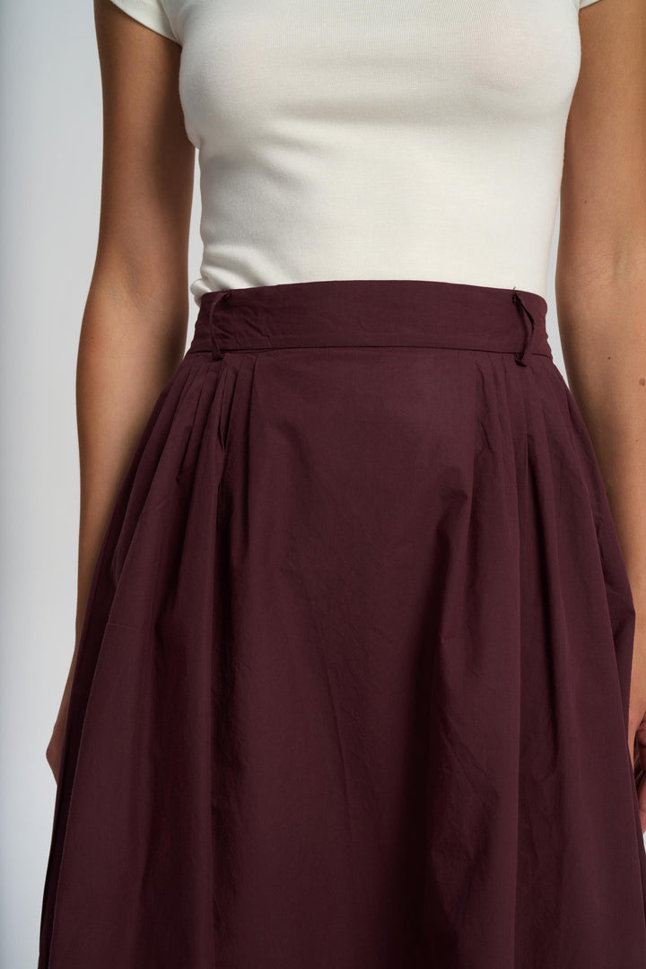 Person wearing a white top and maroon skirt on a plain background