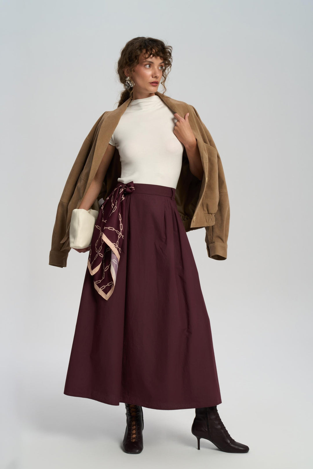 Woman wearing a brown coat, white top, burgundy skirt, and black boots on a white background