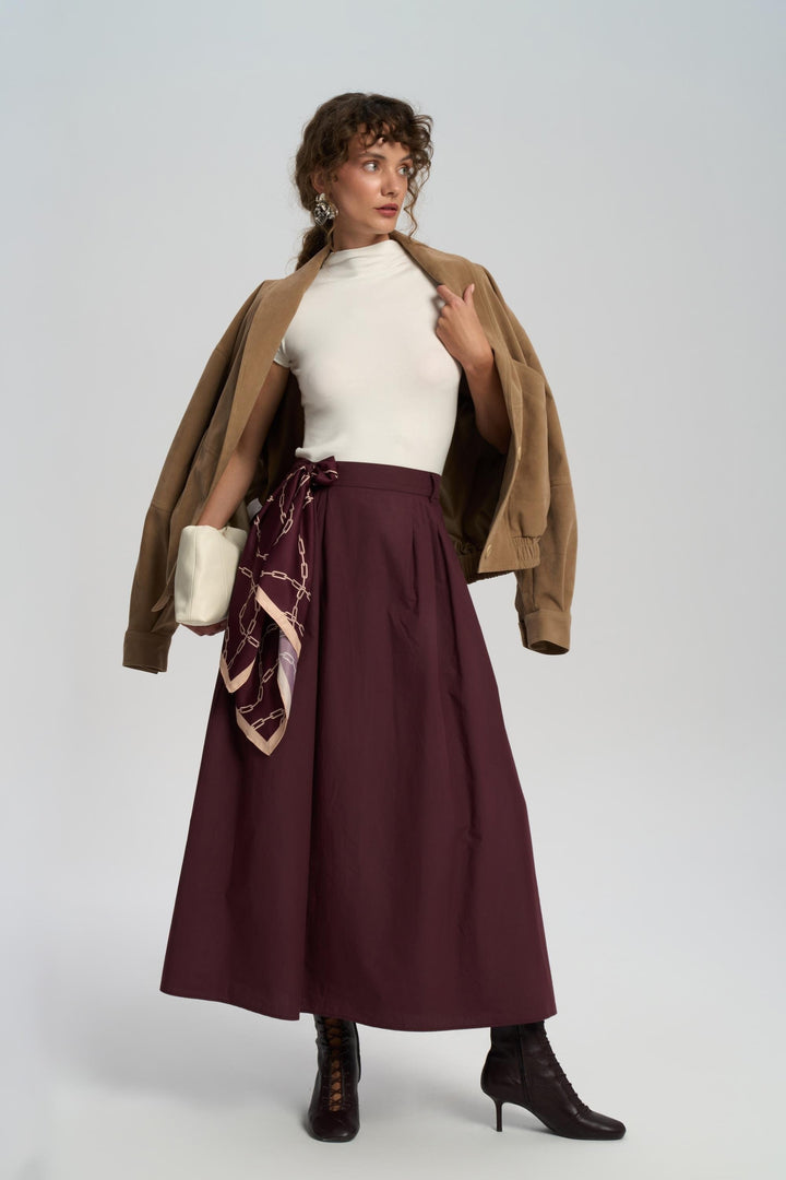 Woman wearing a brown coat, white top, burgundy skirt, and black boots on a white background
