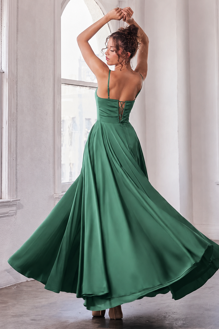 A woman wearing a flowing emerald green maxi dress, captured from behind as she twirls in a bright, sunlit room with high windows.