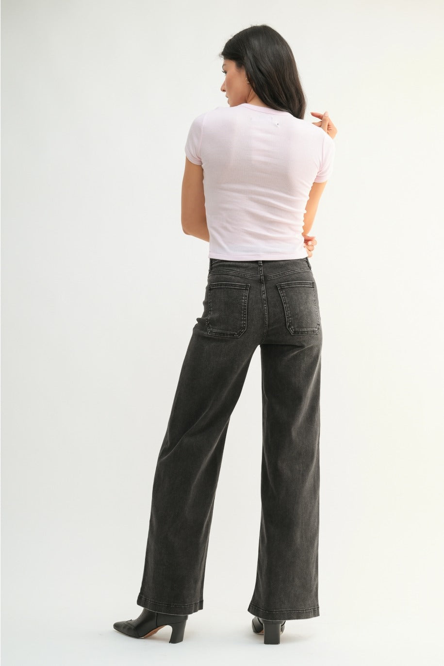 Woman wearing a white top and dark gray wide-leg jeans on a white background