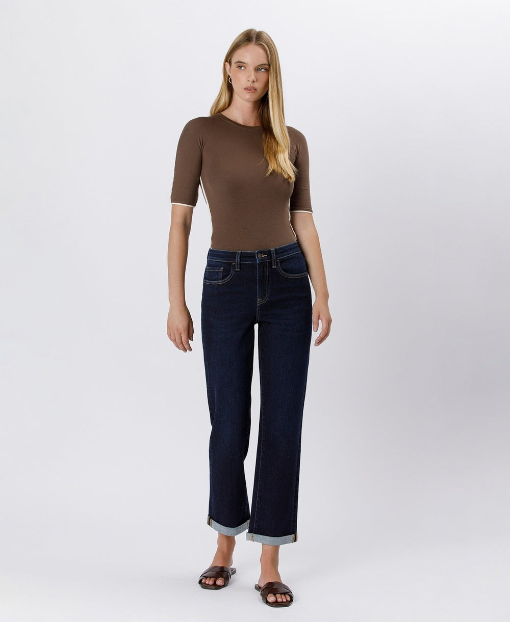 Woman wearing a brown top and dark blue jeans on a white background