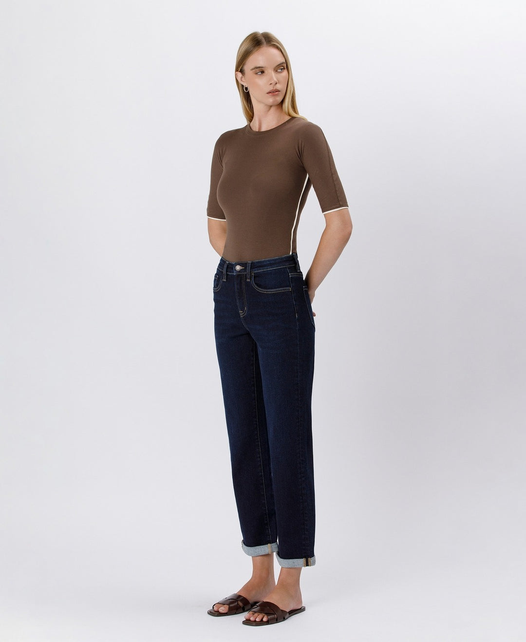 Woman wearing a brown top and dark blue jeans on a white background