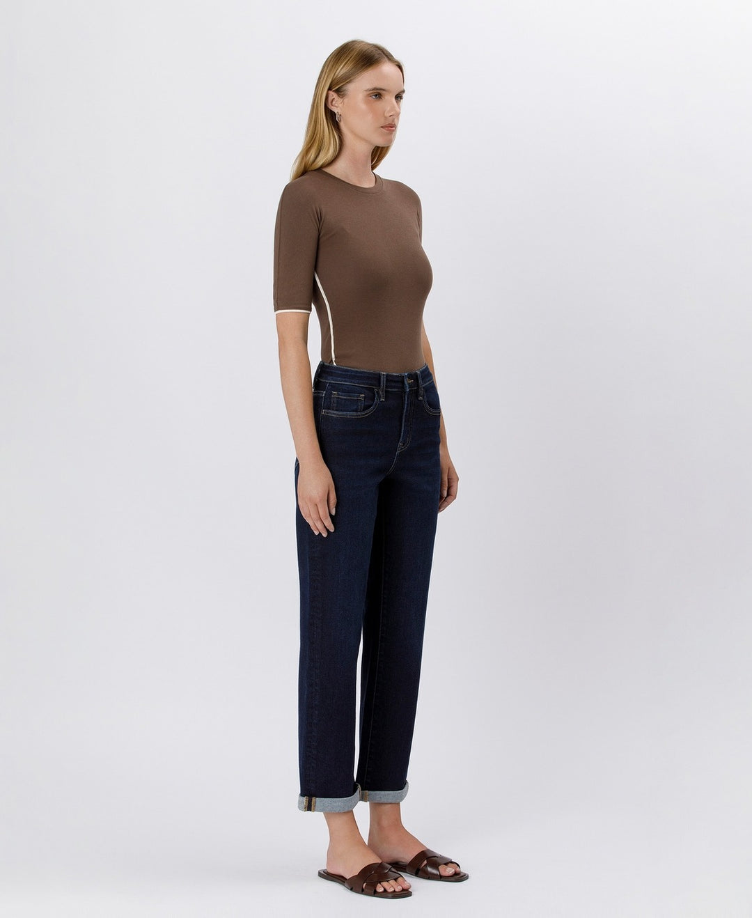 Woman wearing a brown top and dark blue jeans on a white background