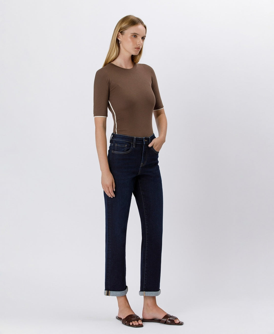 Woman wearing a brown top and dark blue jeans on a white background