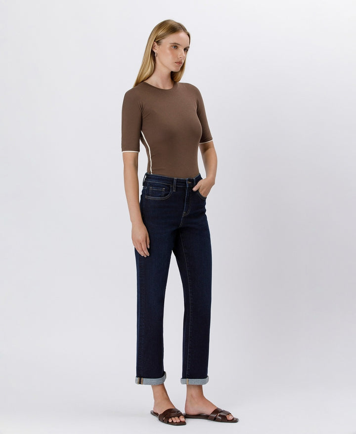 Woman wearing a brown top and dark blue jeans on a white background