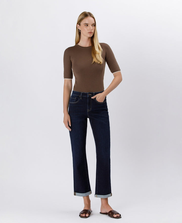 Woman wearing a brown top and dark blue jeans on a white background