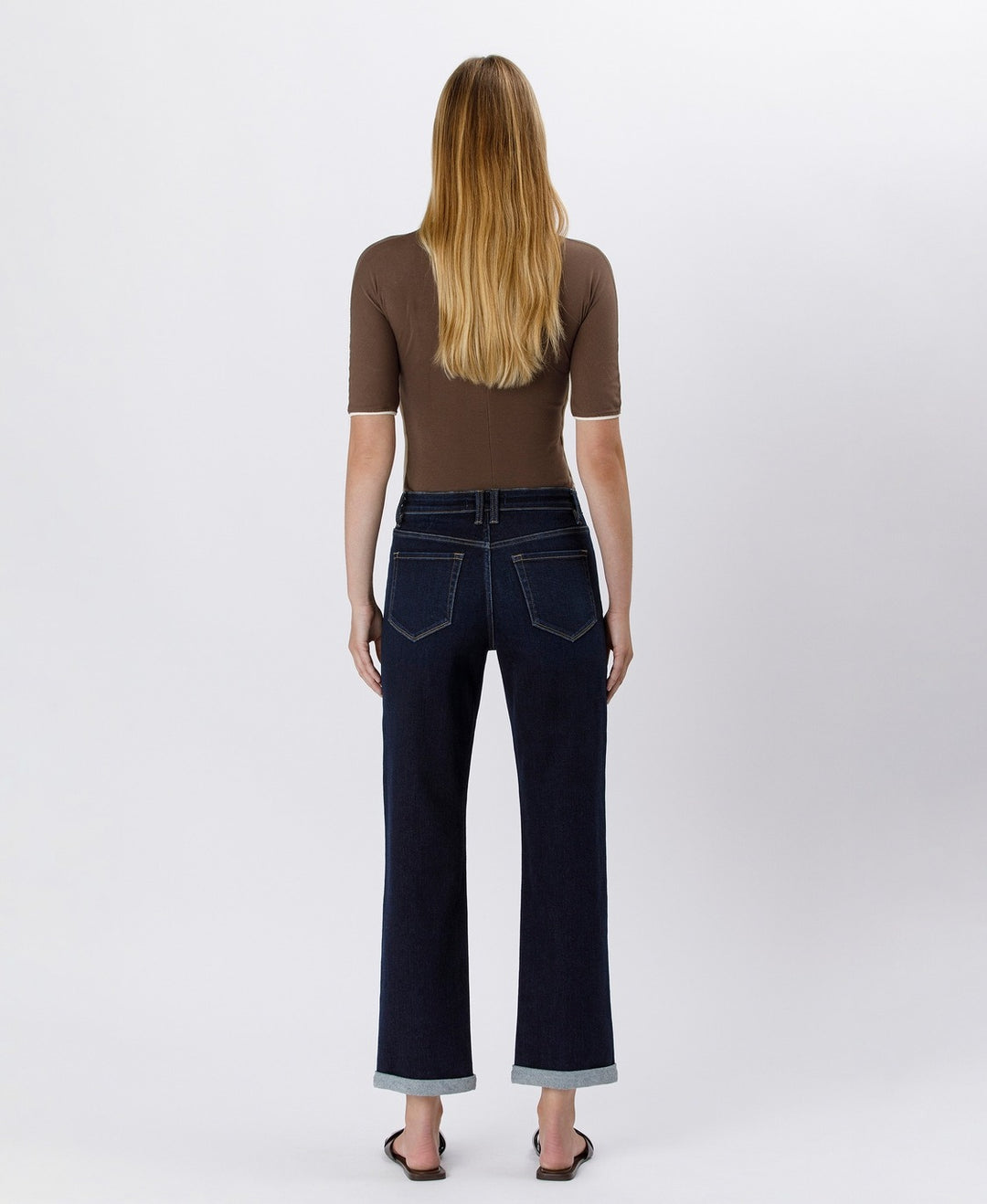 Woman wearing dark blue jeans and a brown top on a white background