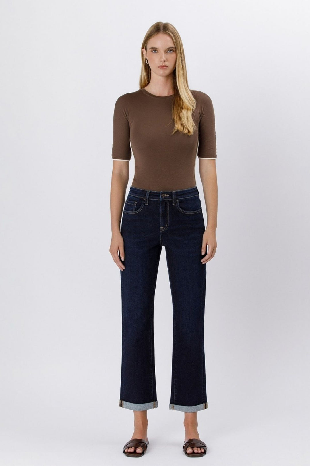 Woman wearing a brown top and dark blue jeans on a white background