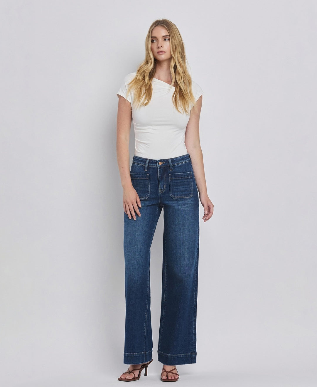 Woman wearing blue jeans and a white top on a plain background