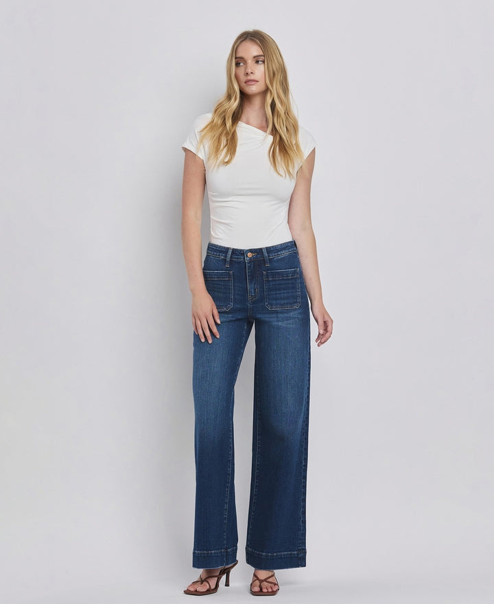 Woman wearing blue jeans and a white top on a plain background