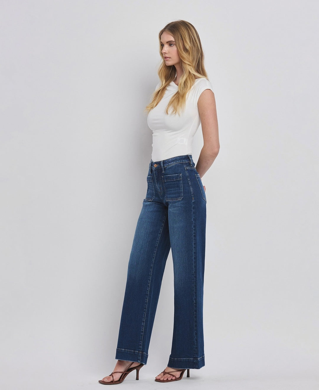 Woman wearing blue jeans and a white top against a plain background