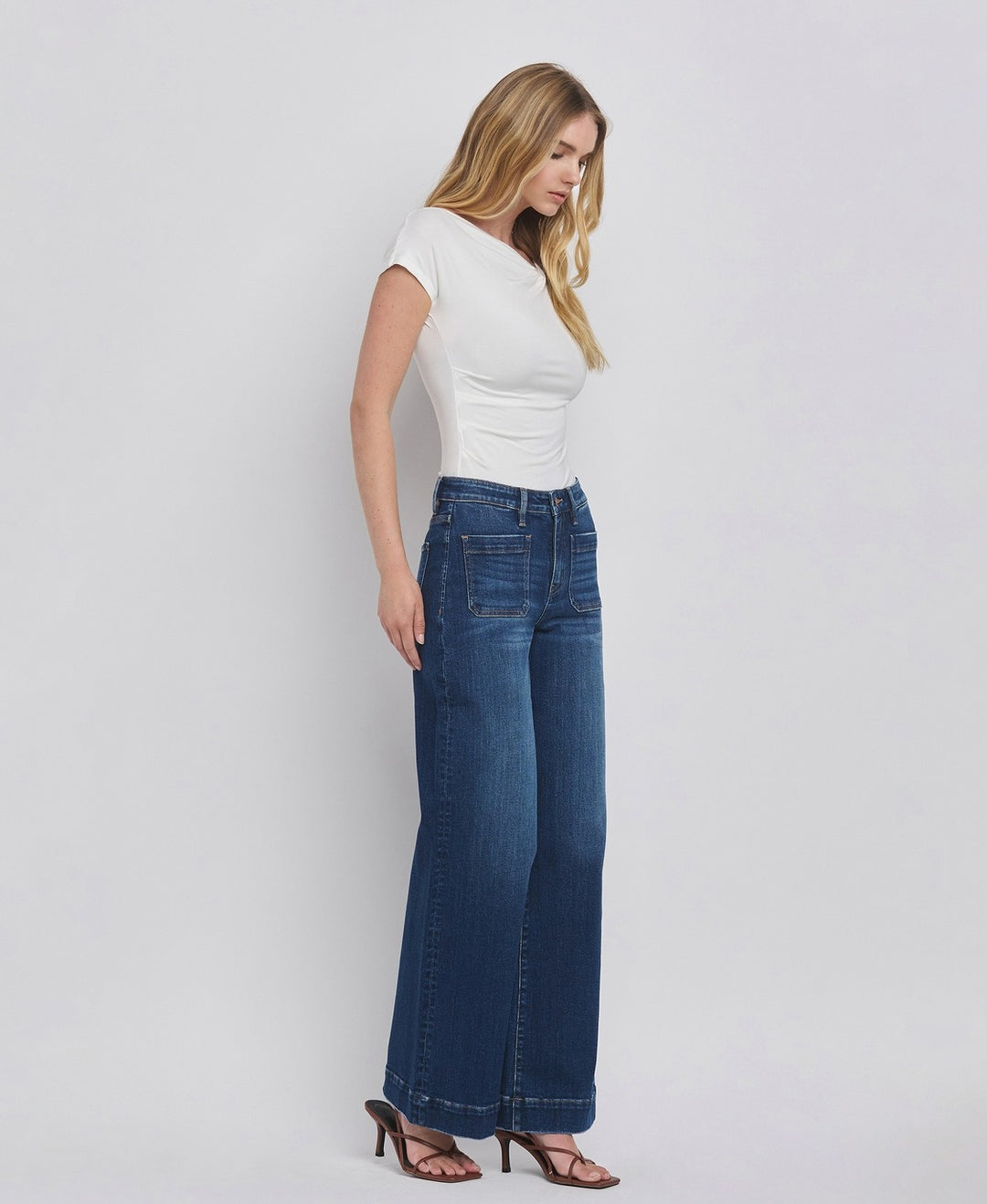 Woman wearing a white top and blue jeans against a plain background