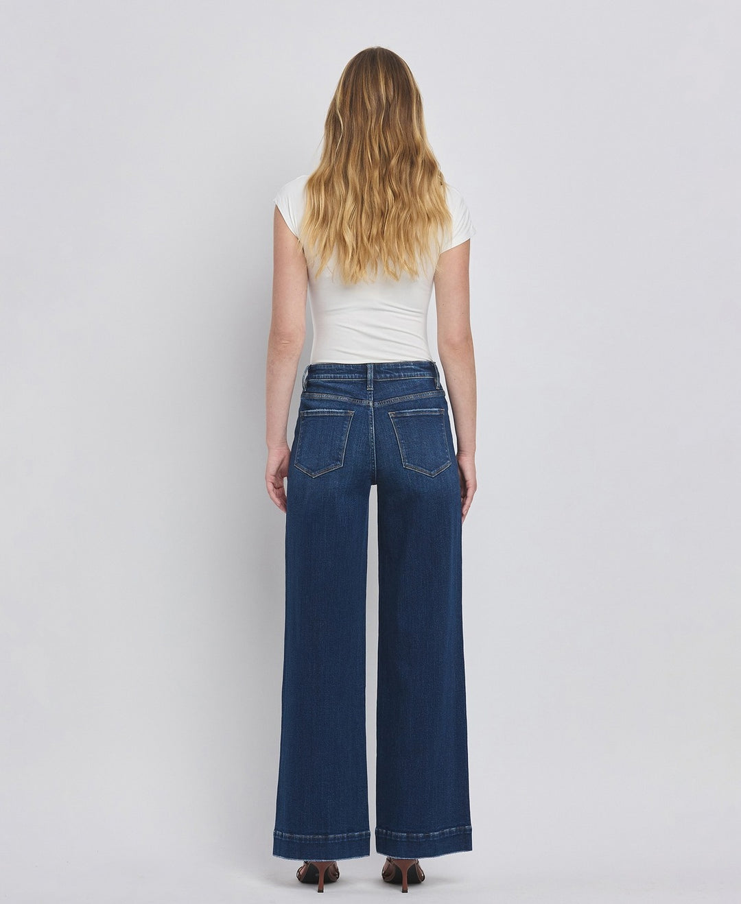 Person wearing blue jeans and a white top on a plain background