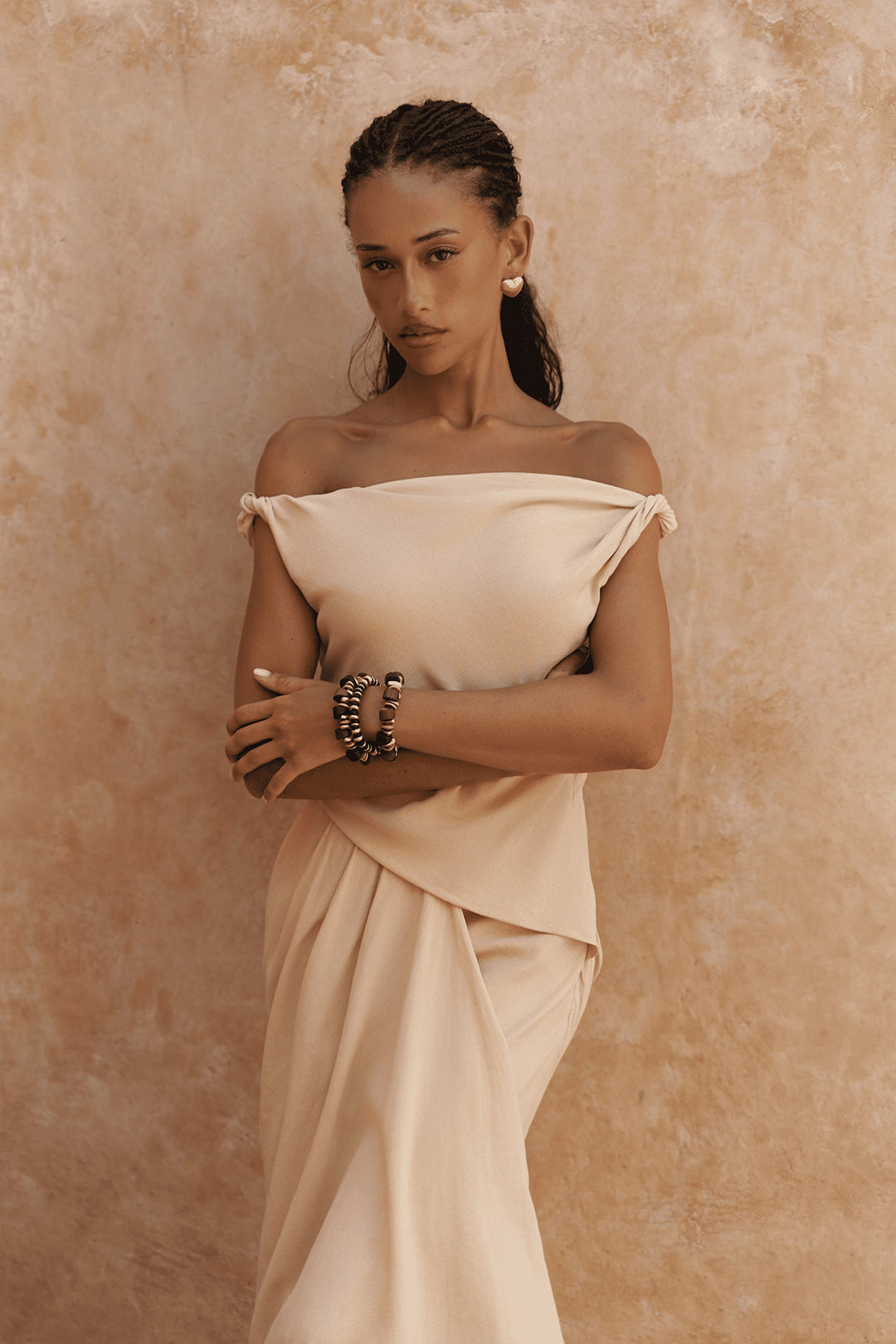 Woman wearing a beige off-shoulder dress against a beige background