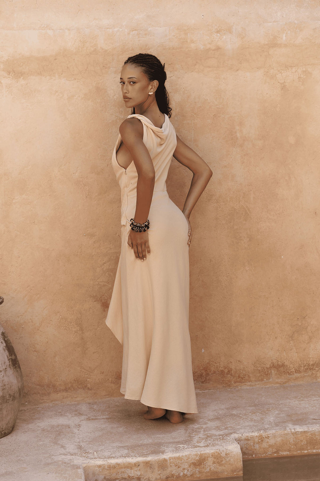 Woman in a beige dress standing against a beige wall