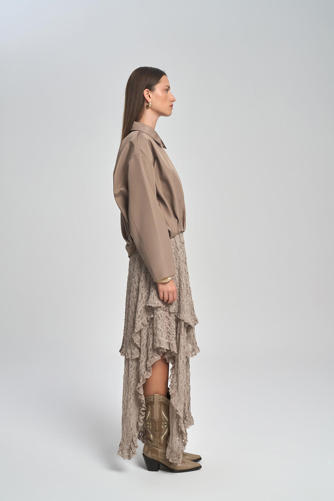 Woman wearing a beige shirt and skirt with brown boots on a white background