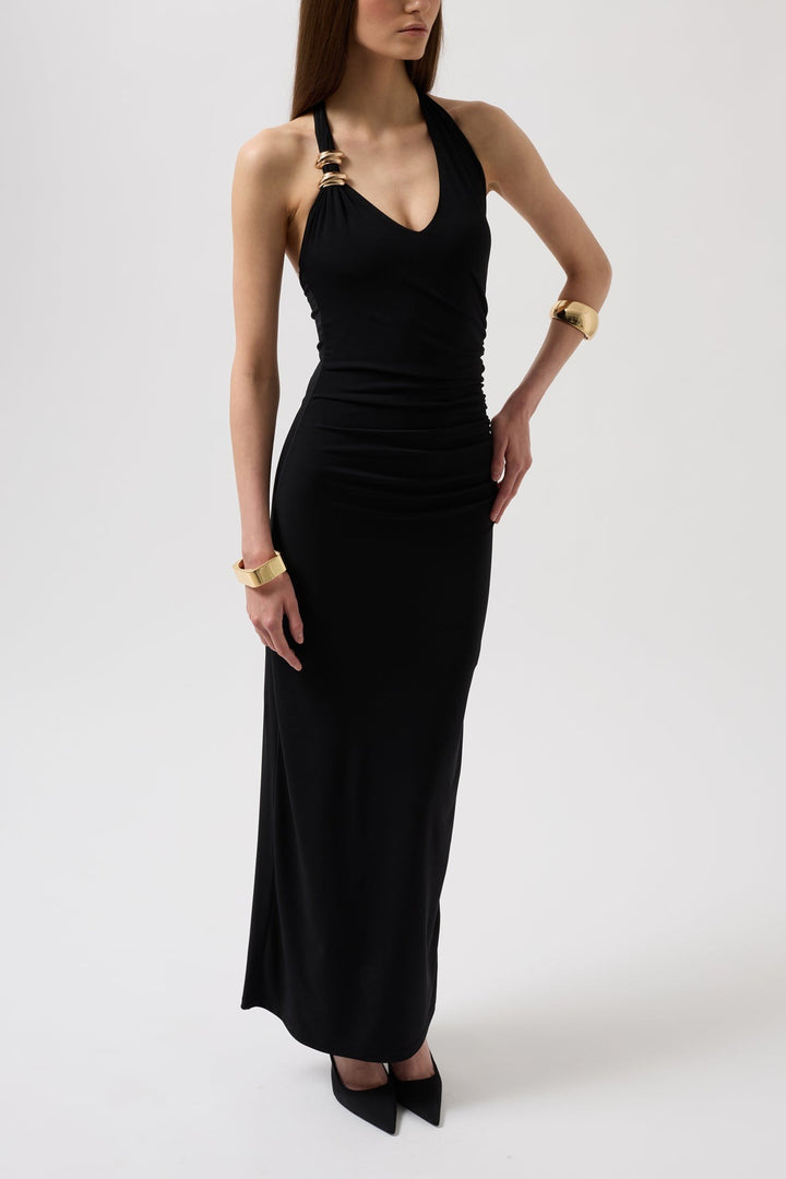 Woman wearing a black halter neck dress with gold accessories on a white background