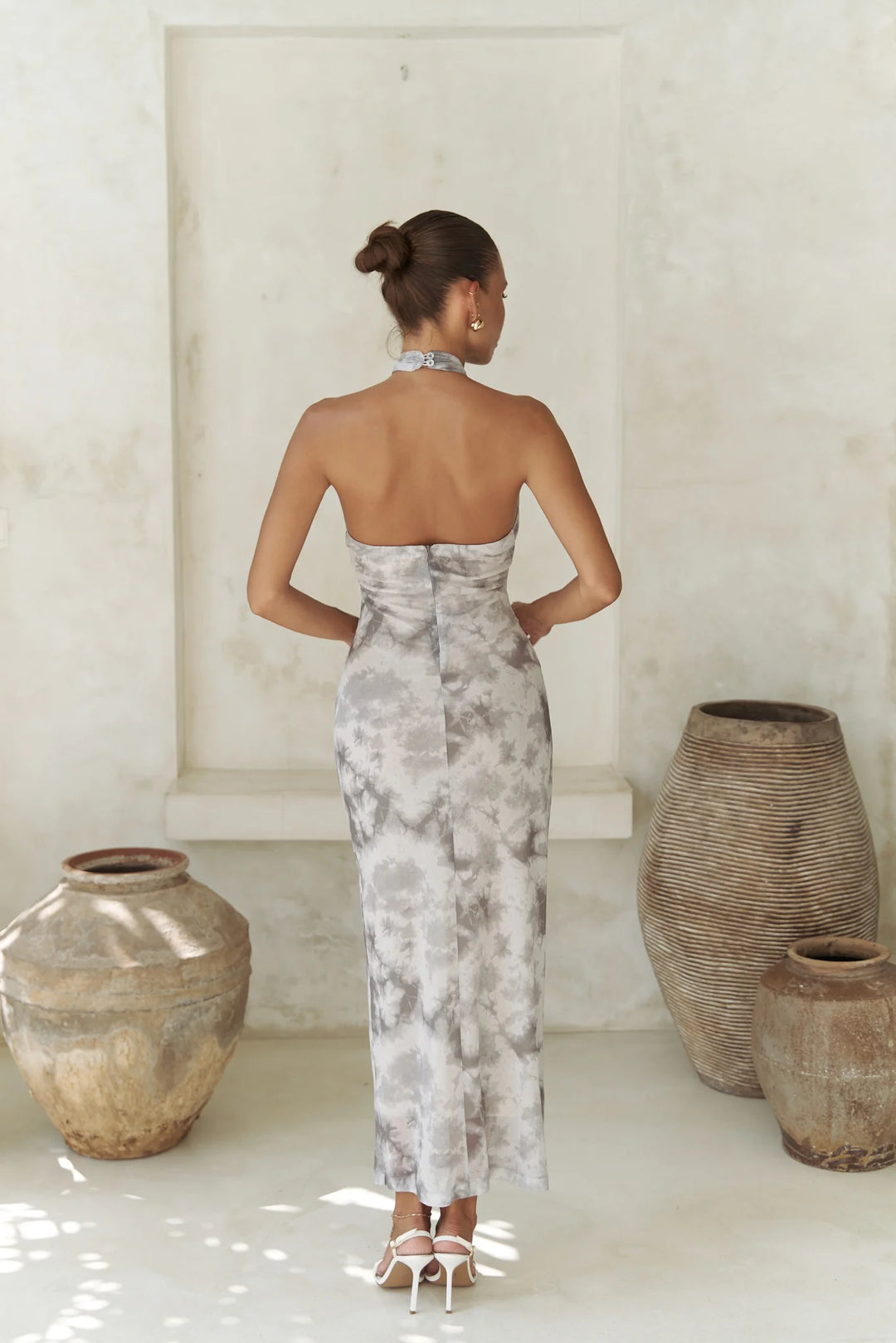 Woman in a floral dress standing in a minimalistic room with large vases.