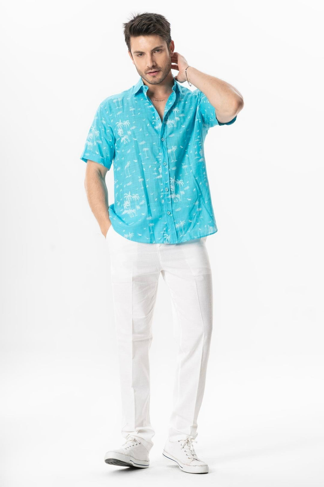 Man wearing a turquoise patterned shirt and white pants on a white background