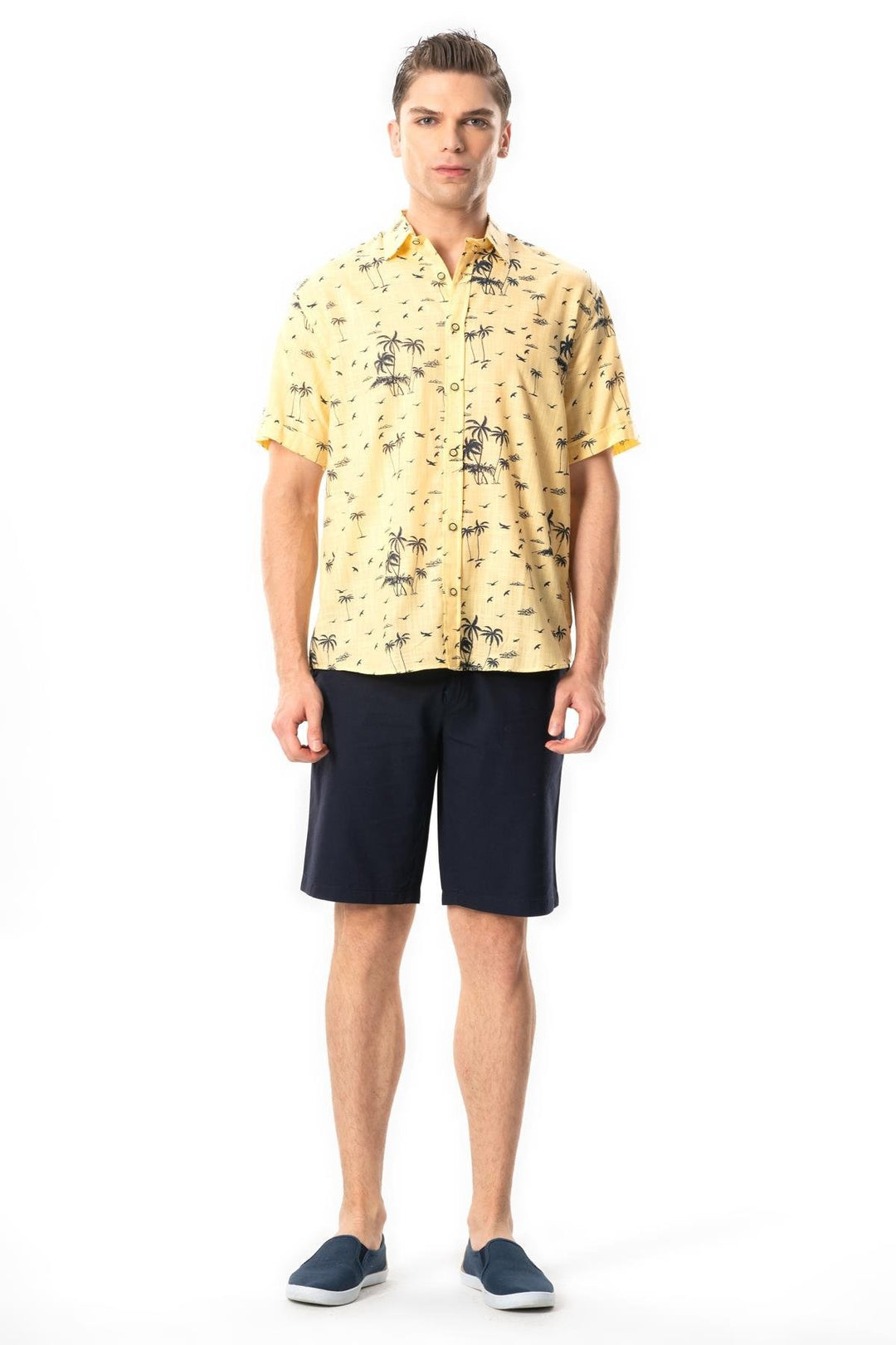 Man wearing a yellow patterned shirt and navy shorts on a white background