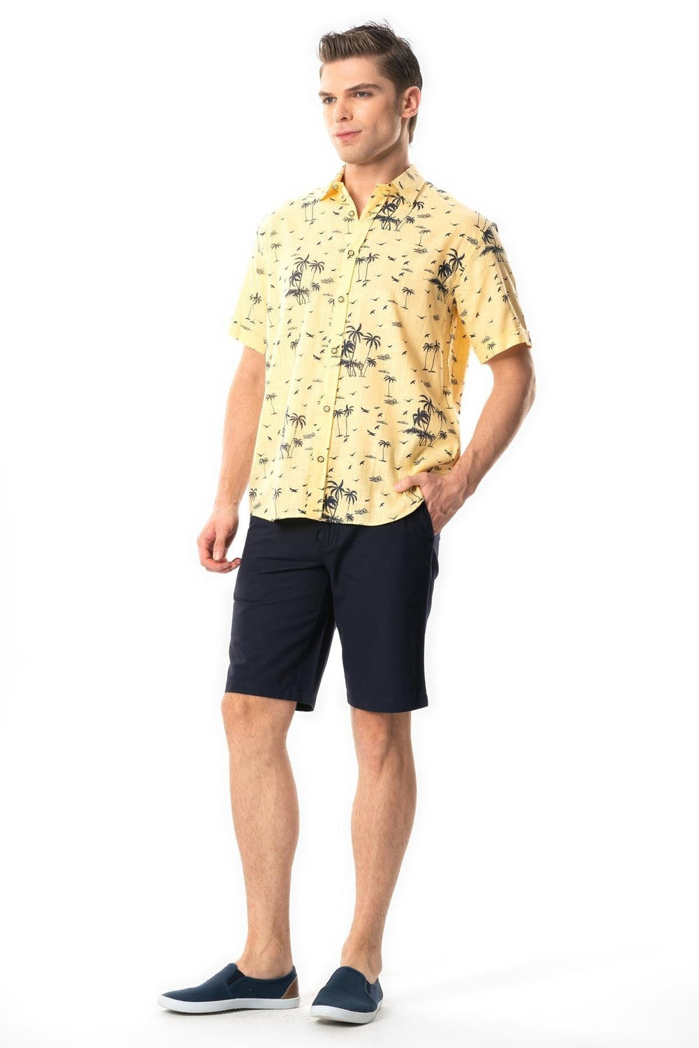 Man wearing a yellow patterned shirt and navy shorts on a white background