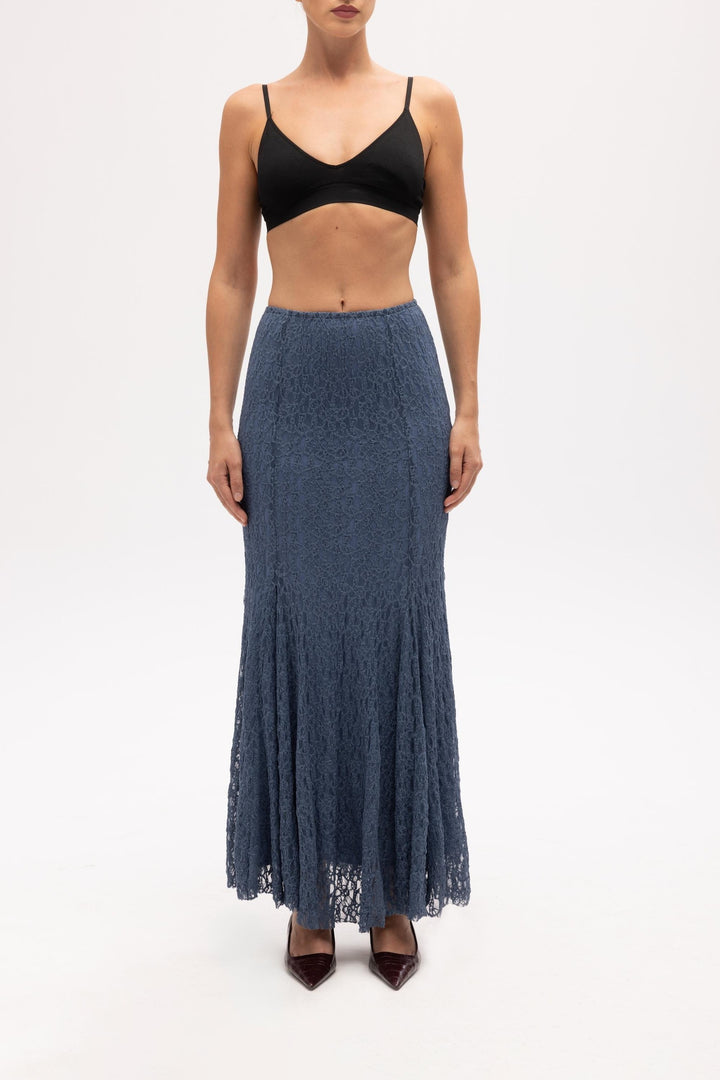 Woman wearing a black top and blue lace skirt on a white background