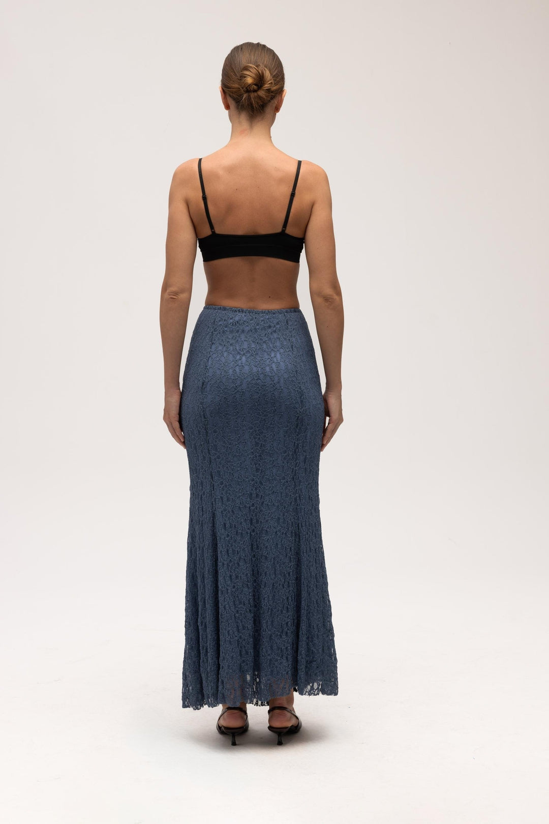 Person wearing a black top and blue lace skirt on a white background