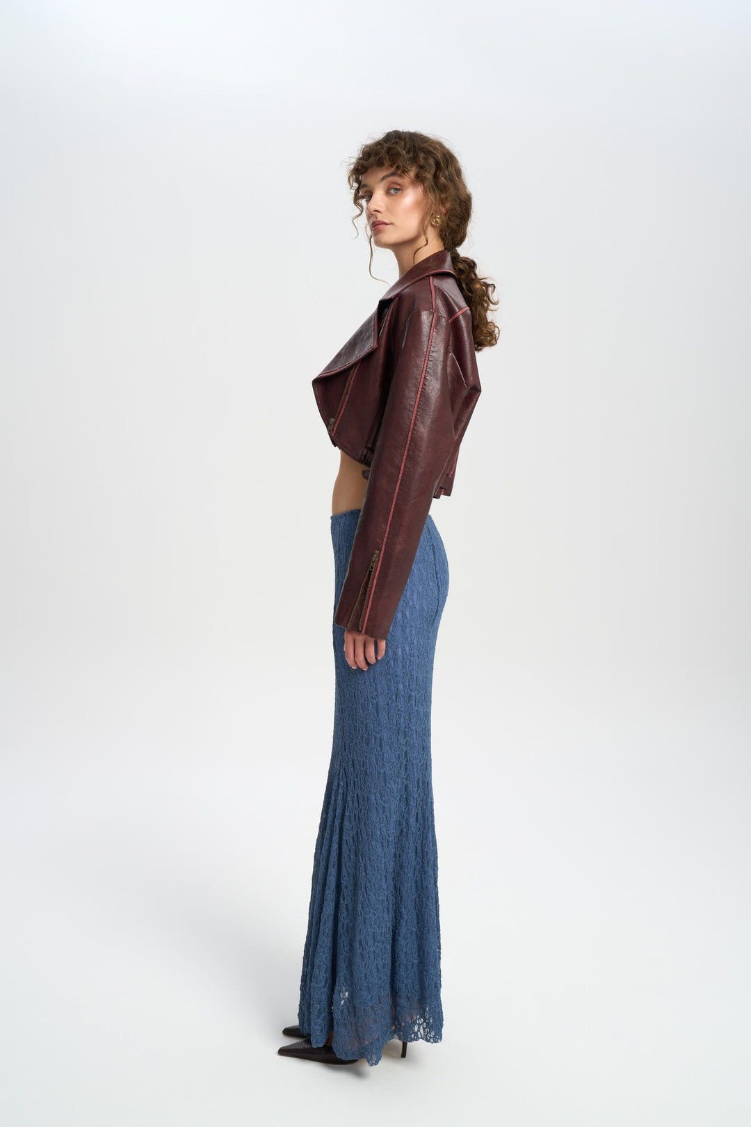 Woman wearing a brown leather jacket and blue denim skirt on a white background