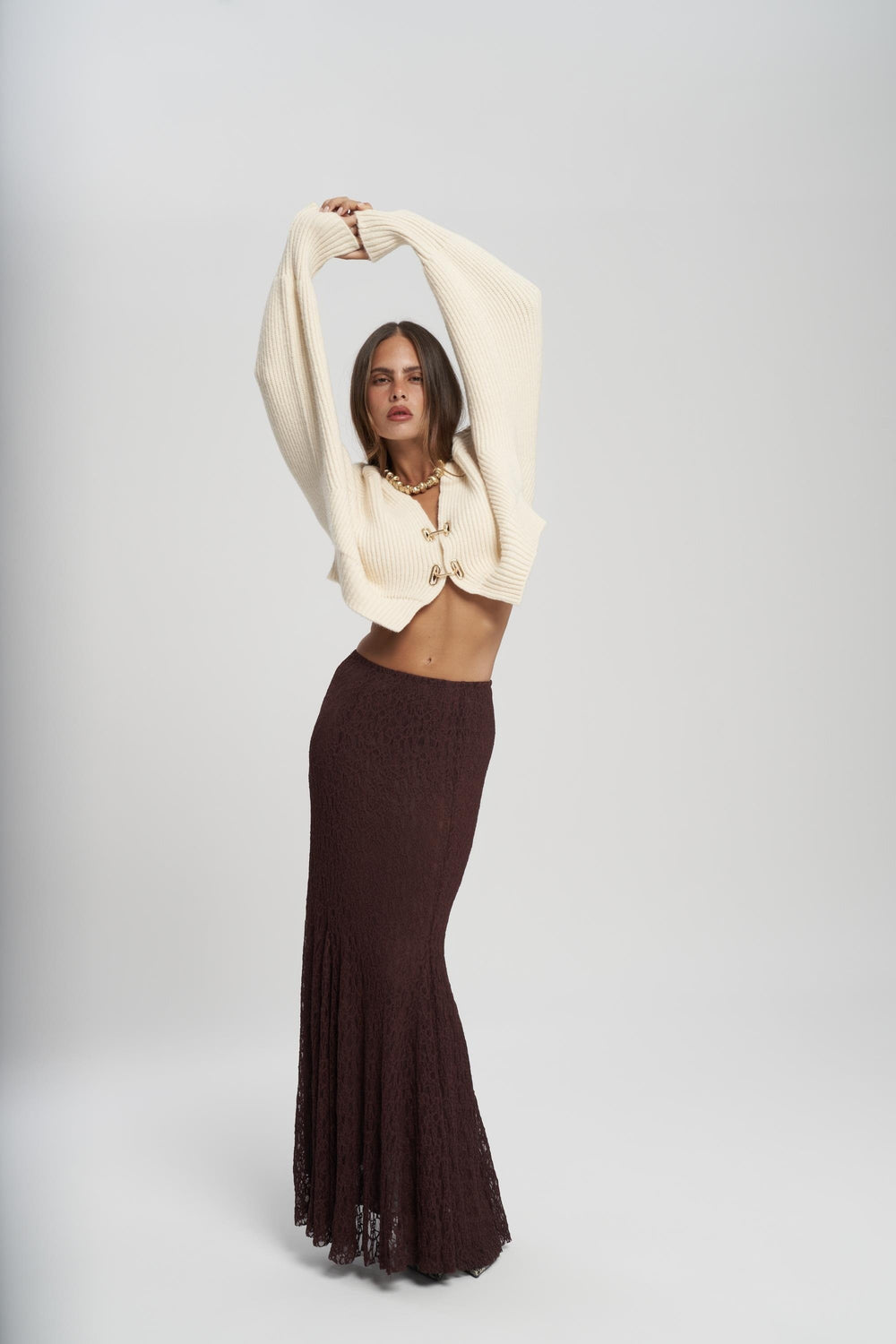 Woman wearing a beige cardigan and dark brown skirt on a white background