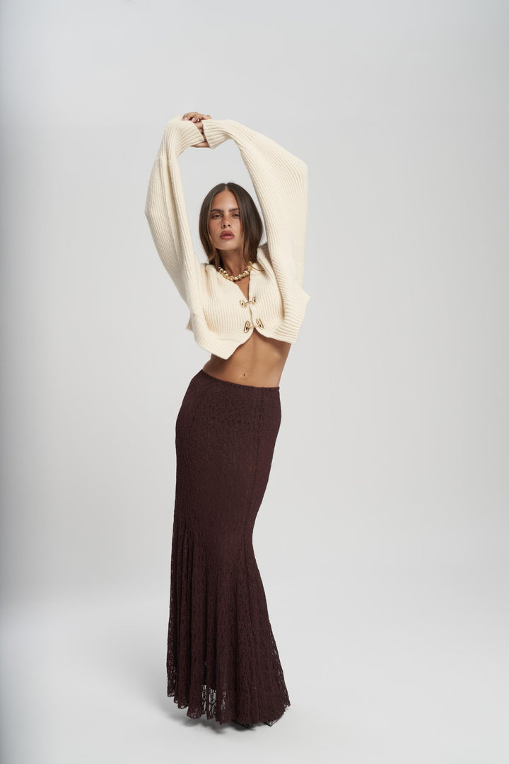 Woman wearing a beige cardigan and dark brown skirt on a white background