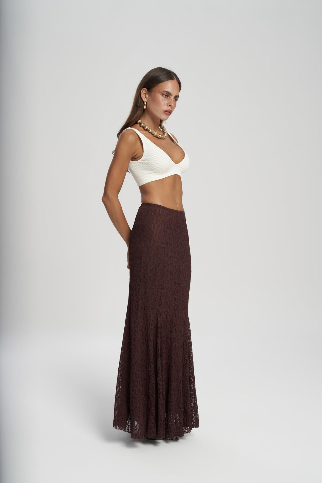 Woman wearing a white top and brown skirt on a gray background