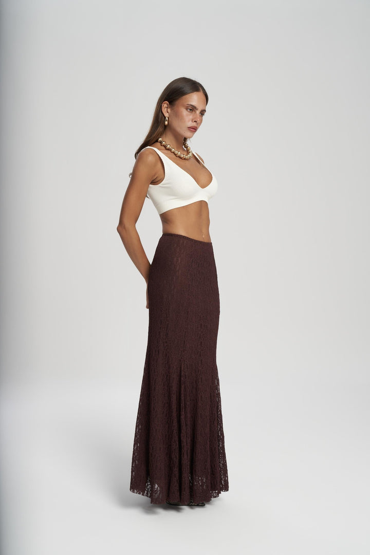 Woman wearing a white top and brown skirt on a gray background