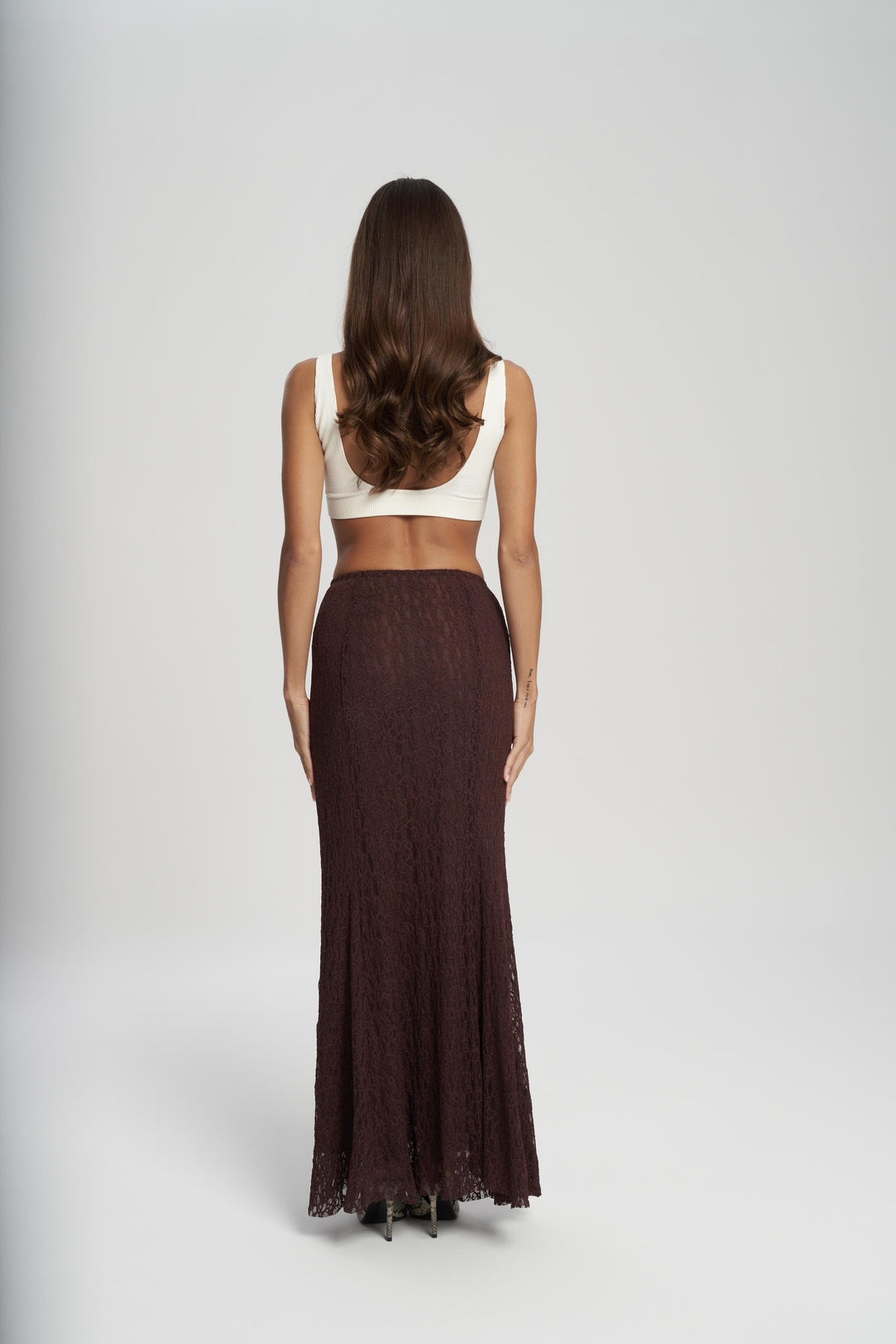 Woman wearing a white top and brown long skirt on a plain background