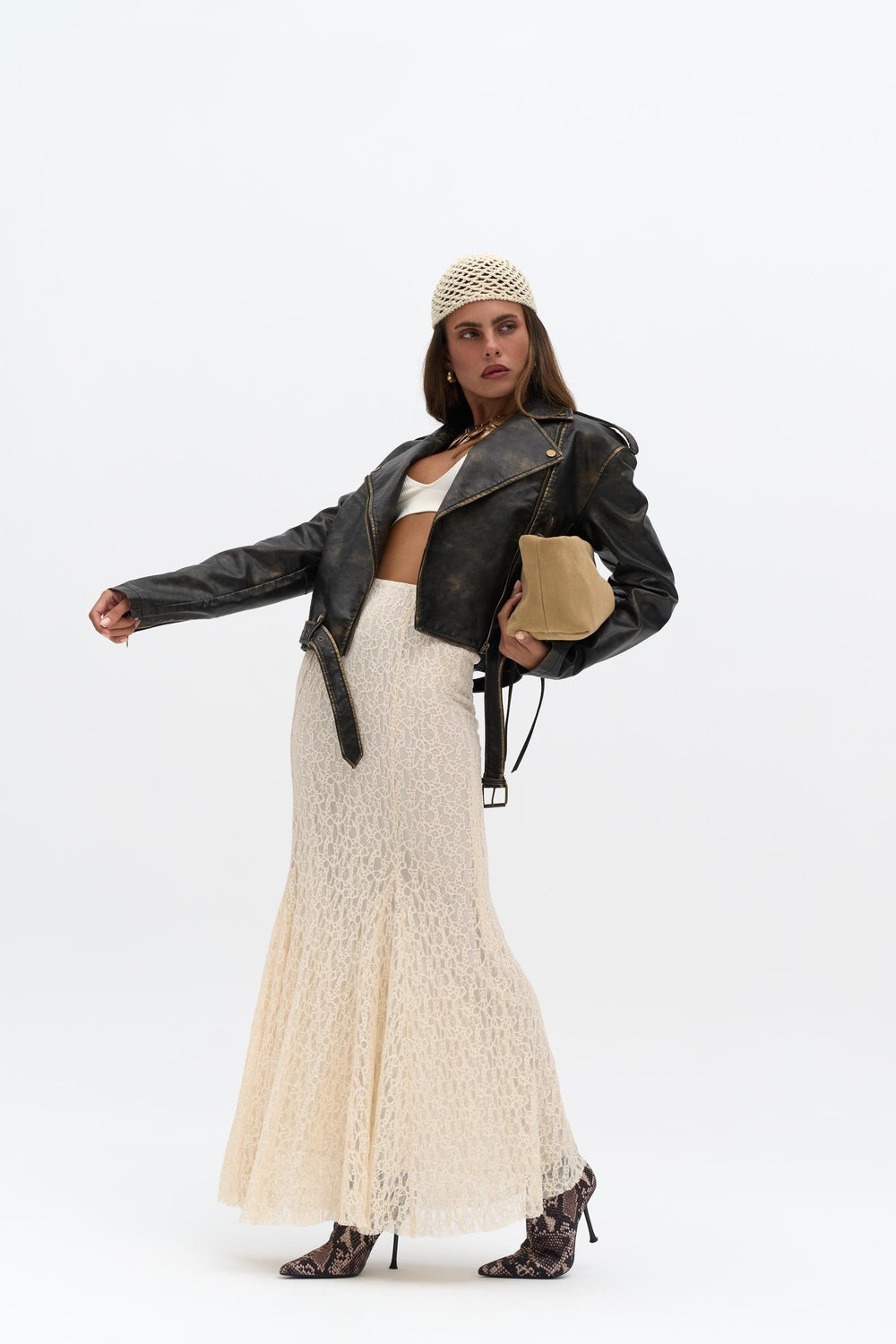 Woman wearing a black leather jacket, white lace dress, and patterned hat on a white background