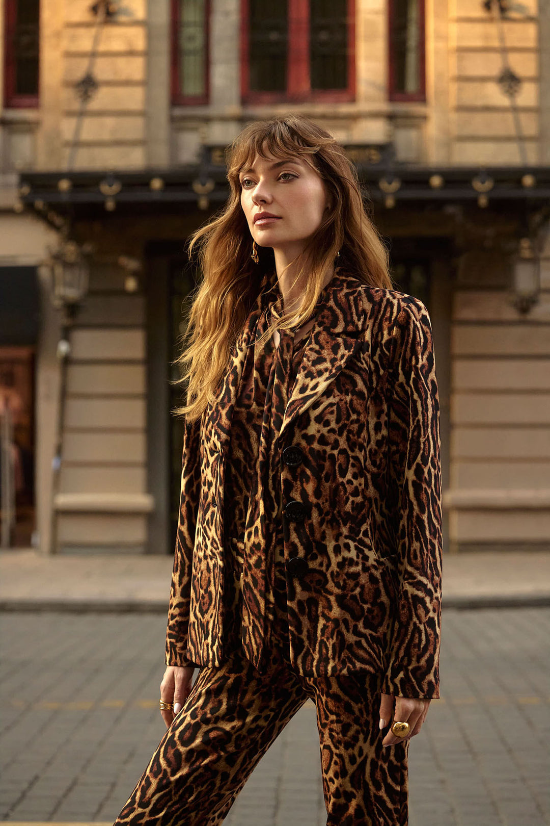 Woman wearing a leopard print suit standing on a street with a building in the background