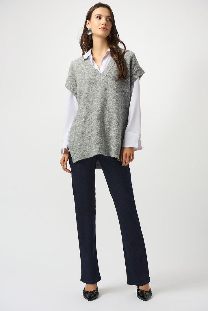 Woman wearing a gray sweater over a white shirt with navy pants on a white background