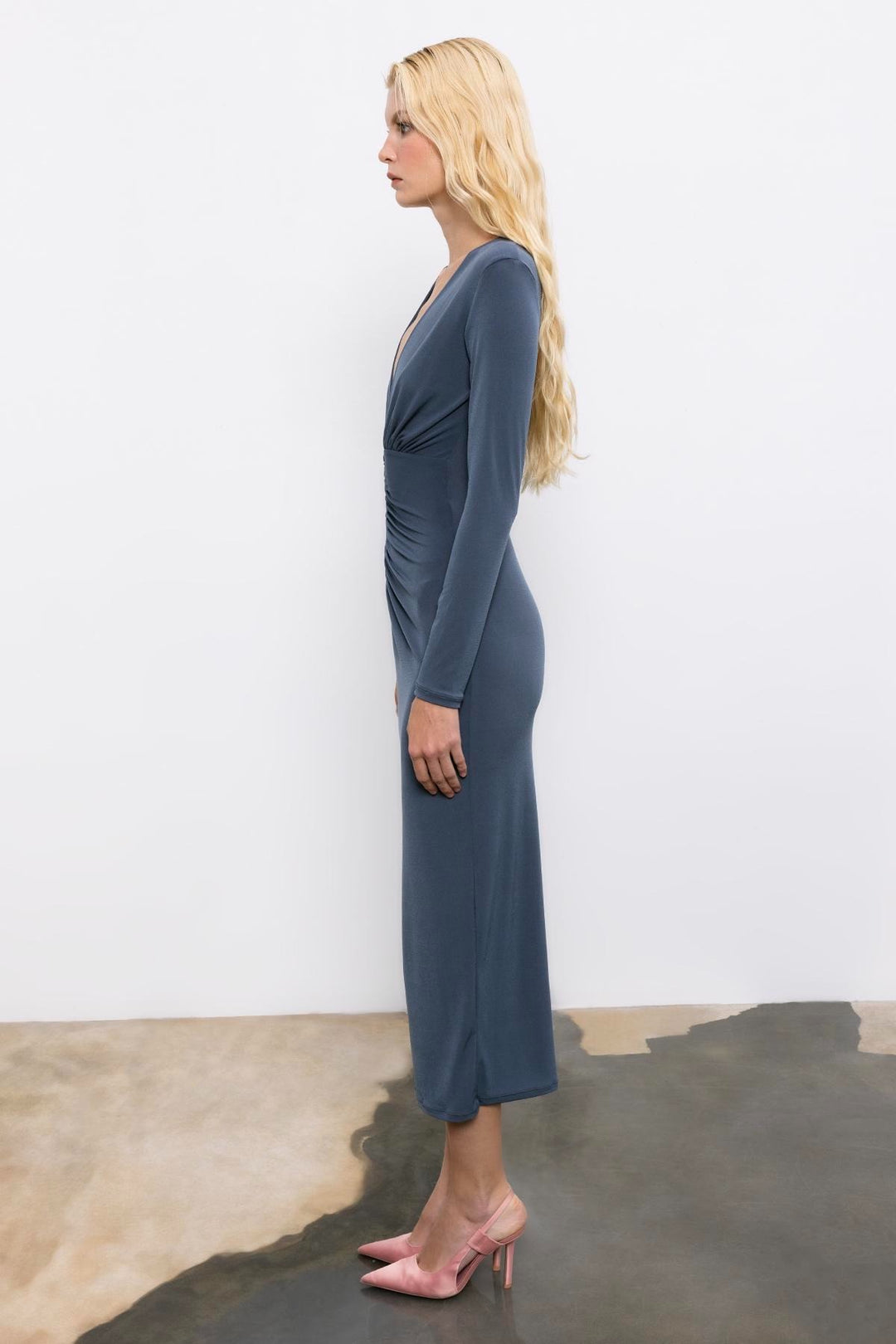 Woman wearing a blue dress standing against a white wall.