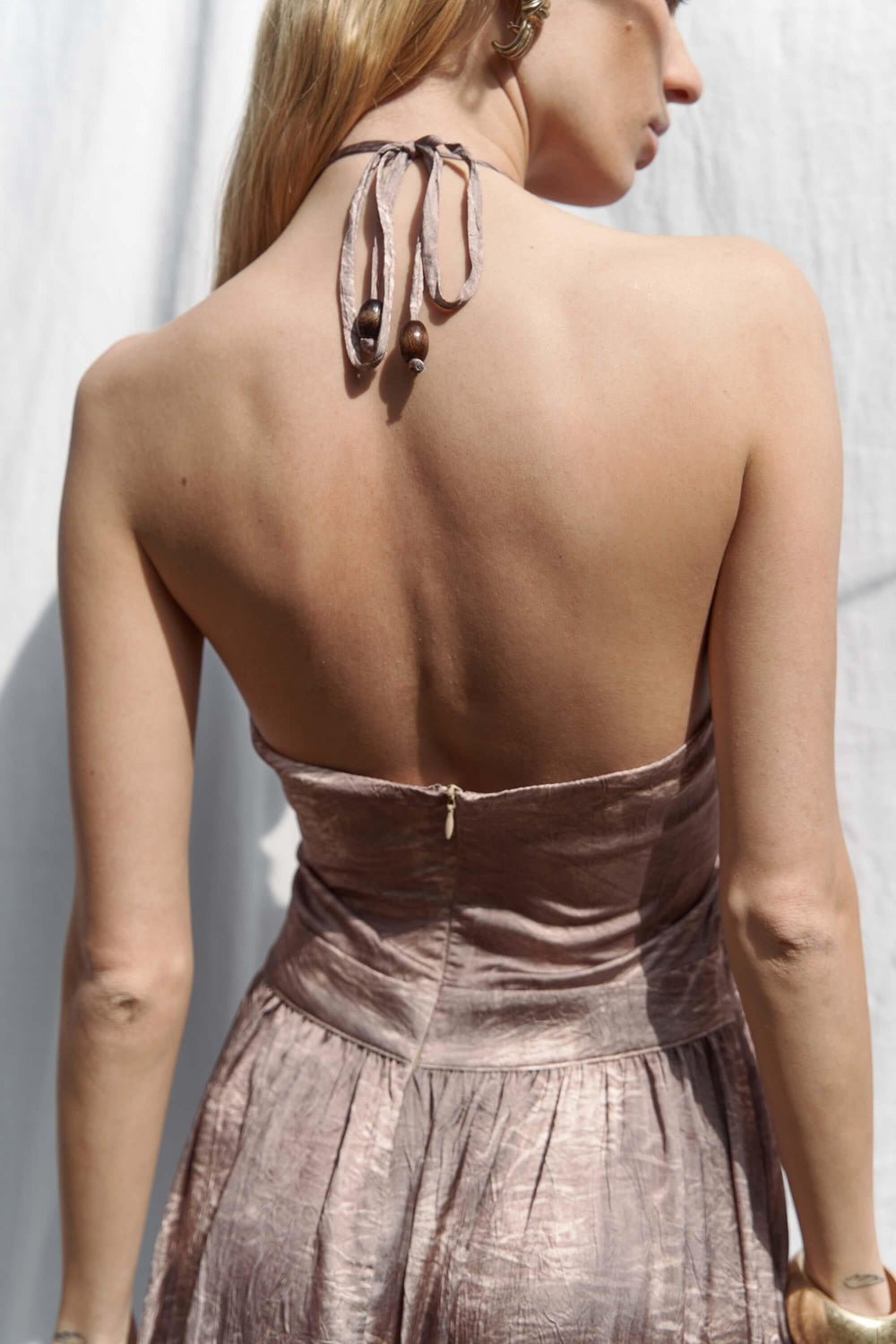 Woman wearing a metallic dress with a backless design against a neutral background
