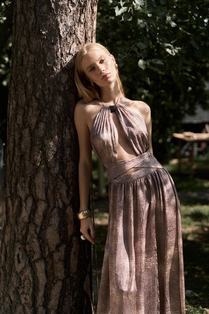 Woman in a long, patterned dress leaning against a tree in a natural setting