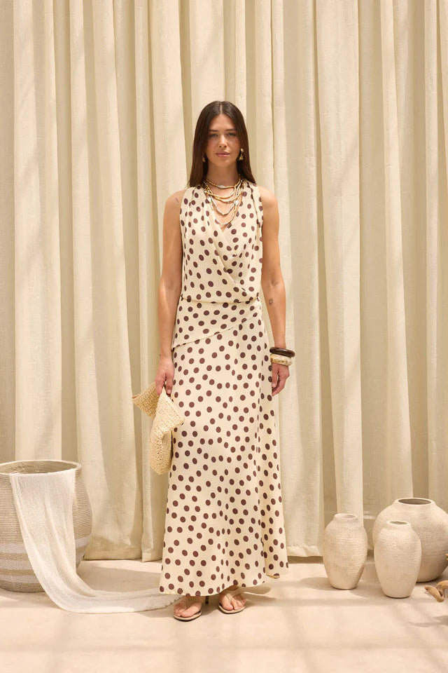 Woman wearing a polka dot dress standing in front of beige curtains with decorative vases on the floor.
