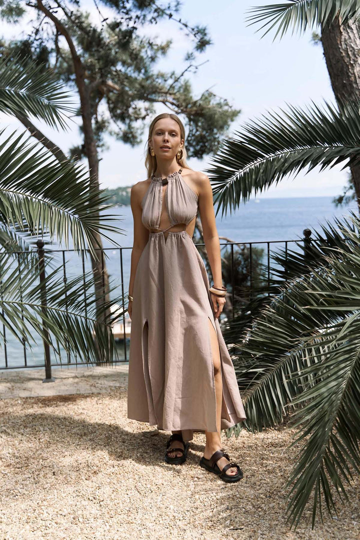 Woman in a beige dress standing among palm trees with a scenic background