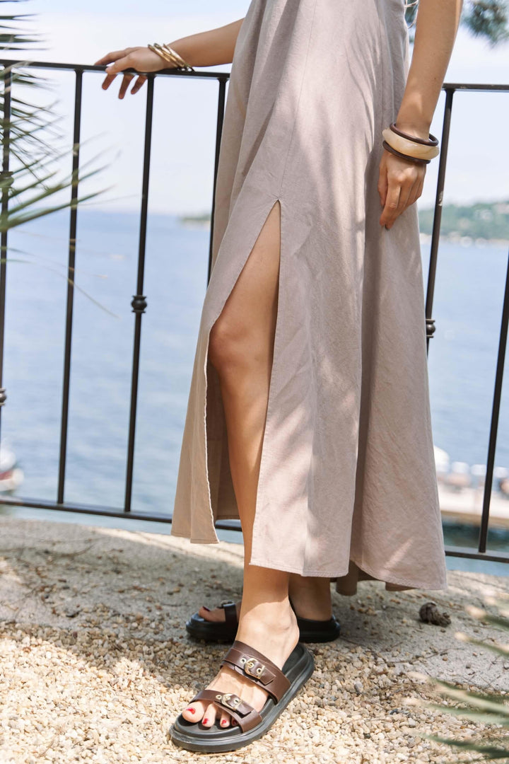 Person wearing a long, light-colored dress with a slit, standing on a balcony with a scenic view.