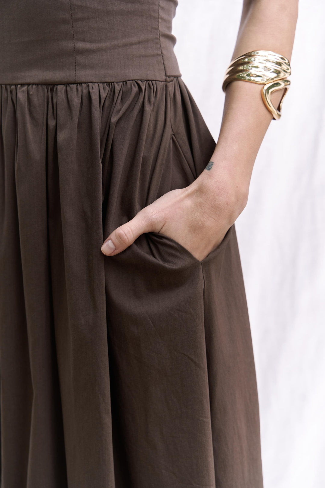 Brown dress with a hand in the pocket against a white background