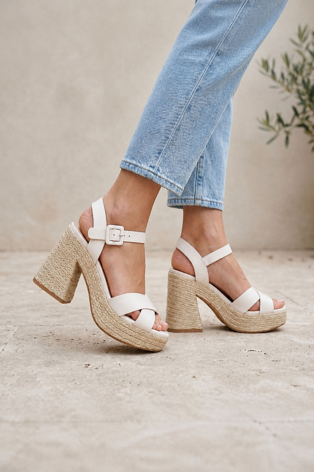 White sandals with block heels worn with light blue jeans on a neutral background