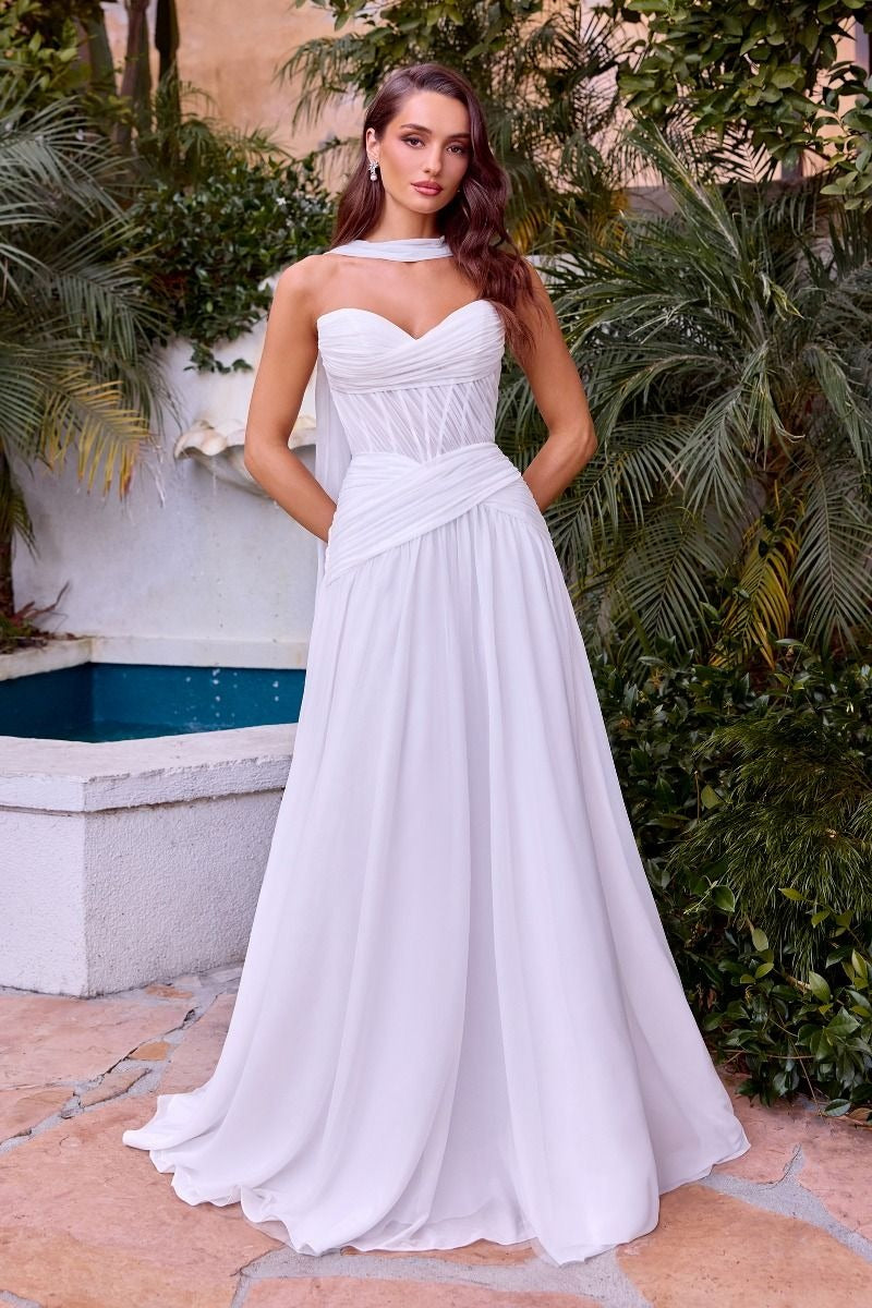 Woman in a white strapless gown standing outdoors with greenery and a fountain in the background