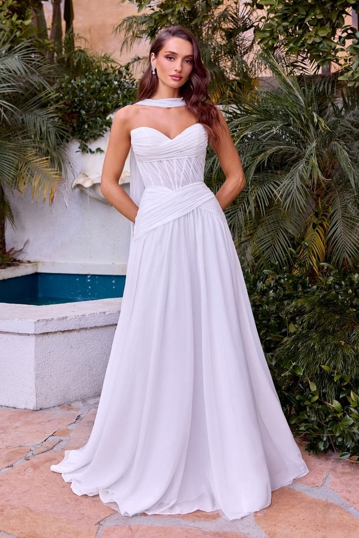 Woman in a white strapless gown standing outdoors with greenery and a fountain in the background